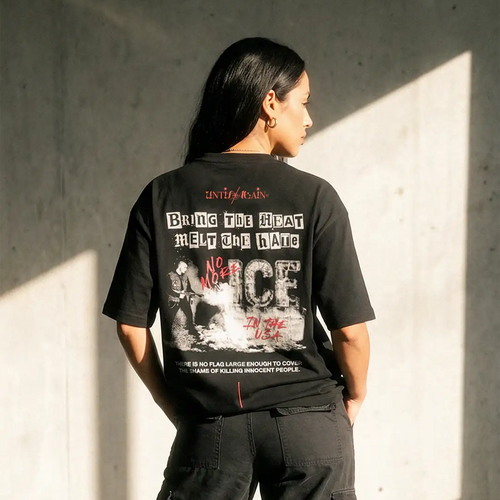 Woman wearing black streetwear graphic tee with bold protest text and cargo pants, sunlight background