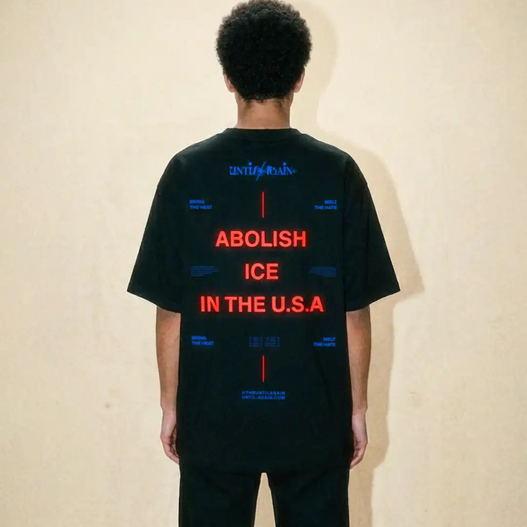 Back view of a person wearing a black streetwear t-shirt with bold red protest text.