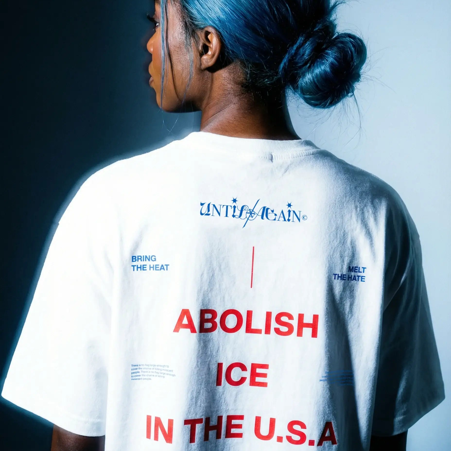 Person with blue hair wearing streetwear t-shirt with activist text, viewed from behind.