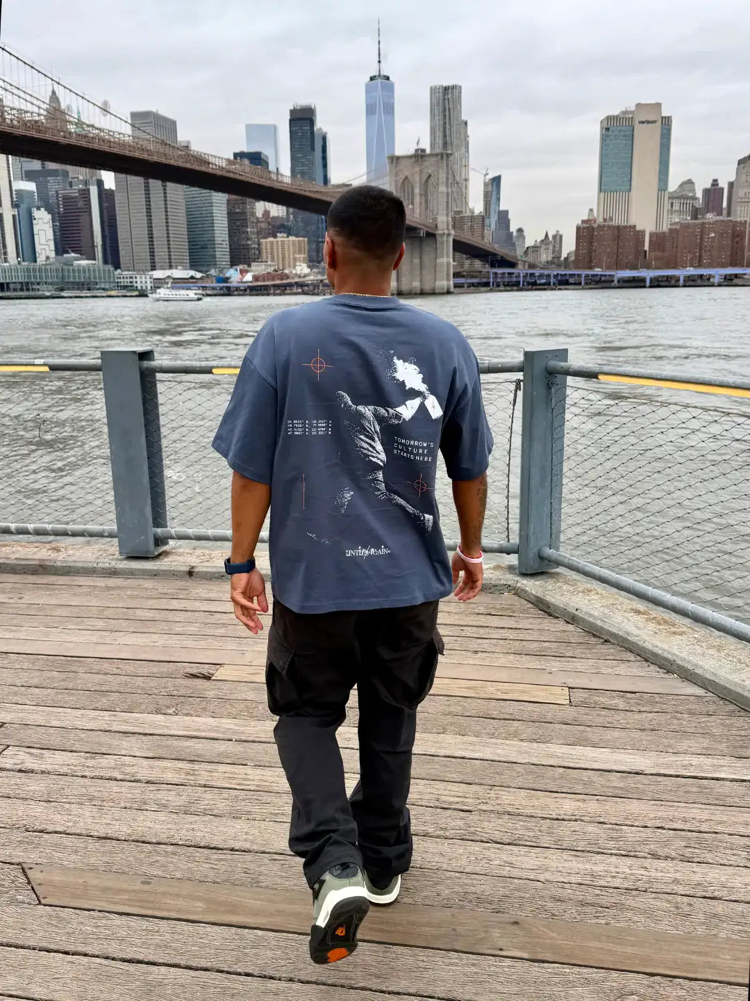 Man wearing graphic streetwear t-shirt and black cargo pants by Brooklyn Bridge skyline