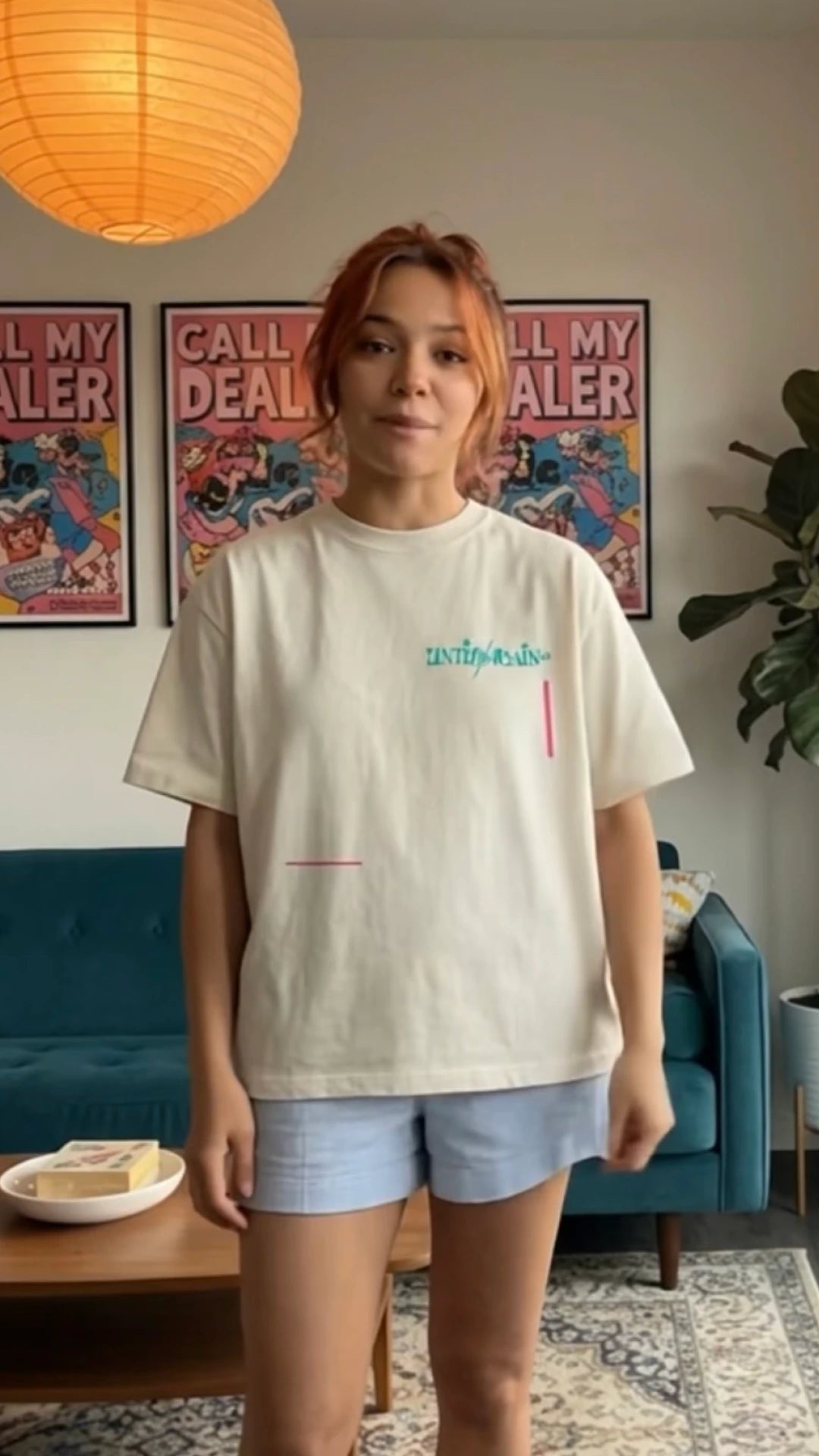 Person wearing UNTIL/AGAIN limited drop cream tee with logo in a modern living room.
