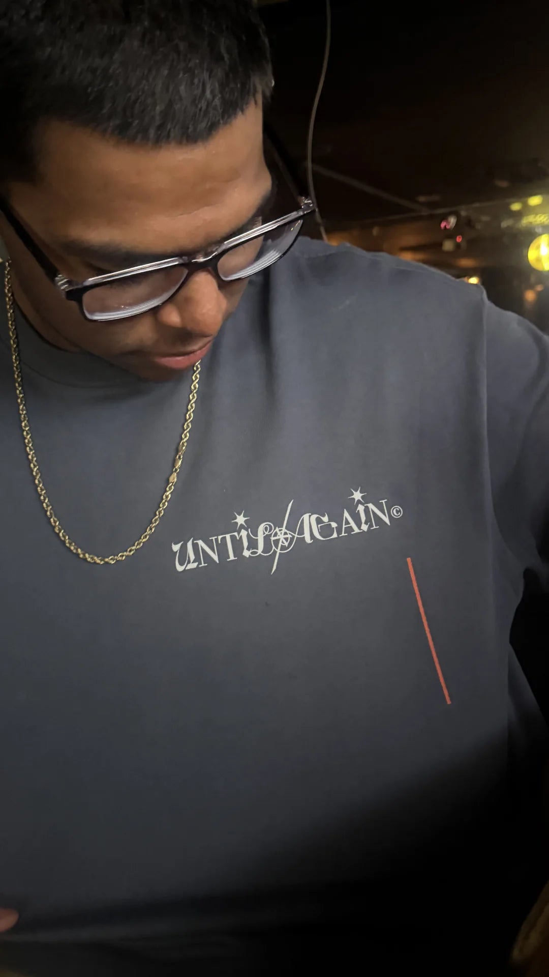 Person wearing a dark gray sweatshirt with 'UNTIL AGAIN' text, standing against a blurred background.