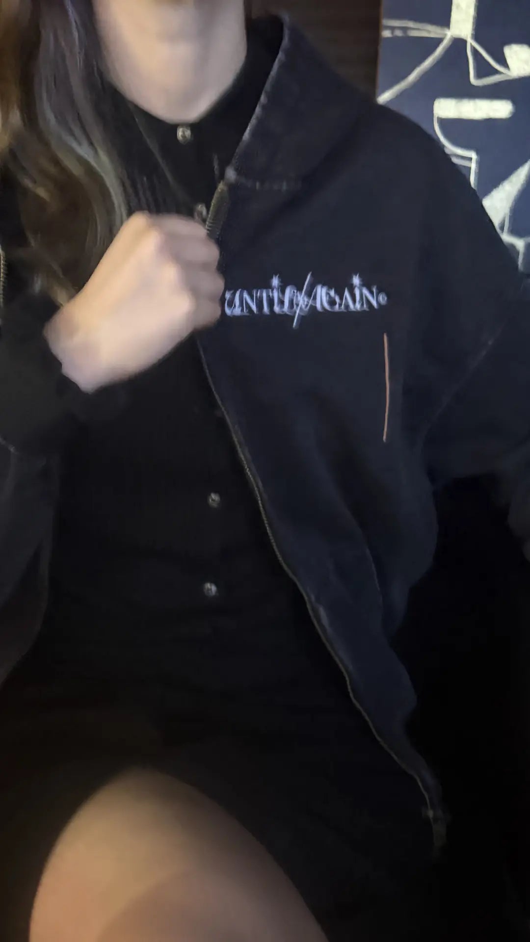Person wearing a UNTIL/AGAIN limited drop black jacket with white logo embroidery