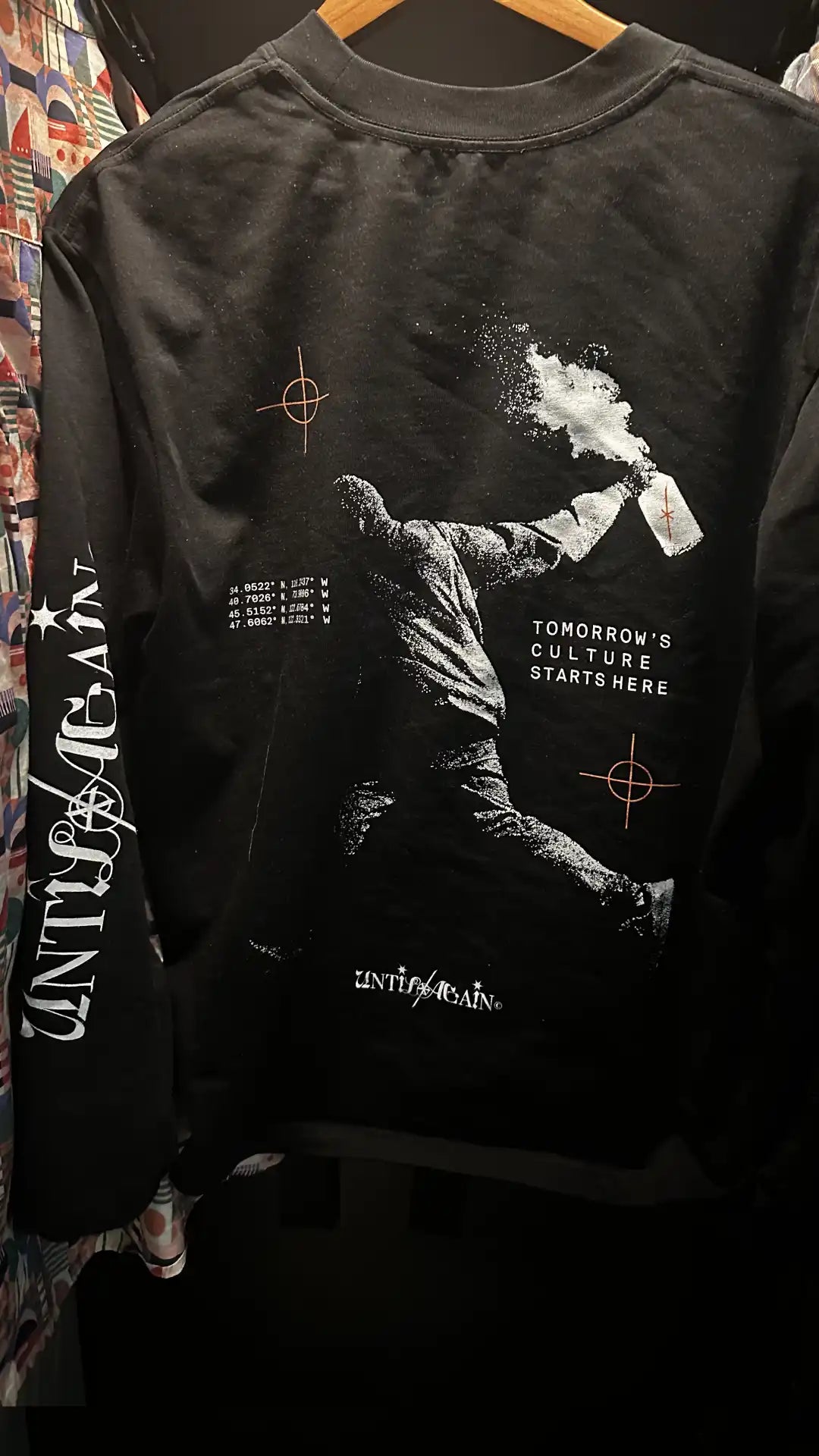 Black UNTIL/AGAIN limited drop long sleeve shirt with graphic of figure spray painting and bold typography.