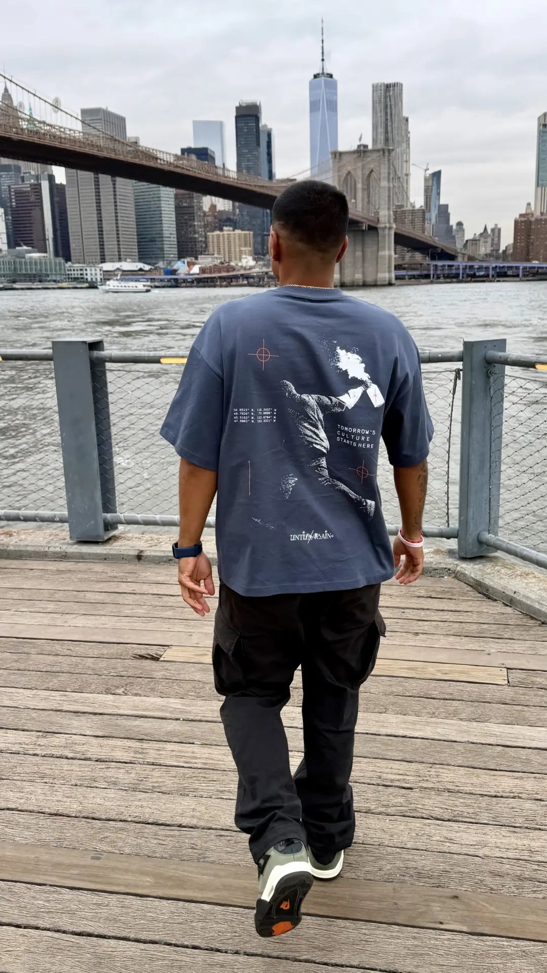 Man wearing UNTIL/AGAIN limited drop graphic tee by the Brooklyn Bridge, New York City.