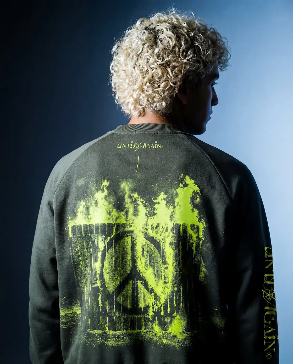 Man in streetwear sweatshirt with neon yellow flaming peace sign graphic and curly blond hair