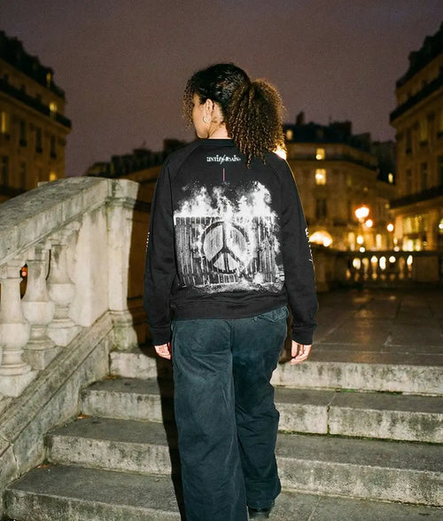 Person in streetwear sweatshirt with peace symbol and flames graphic, standing on city steps at night