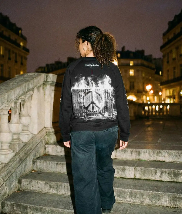 Person in streetwear sweatshirt with peace symbol and flames graphic, standing on city steps at night