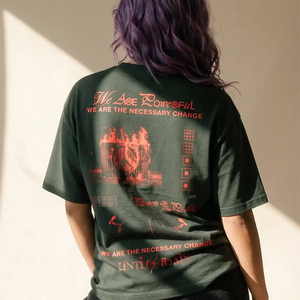 Person with purple hair wearing a graphic streetwear t-shirt featuring bold red text and peace symbol on the back.