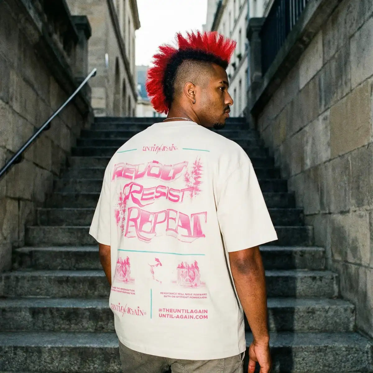 Man with red mohawk wearing graphic streetwear t-shirt on outdoor stone stairs Resist Repeat T Shirt beige on body back graphic streetwear