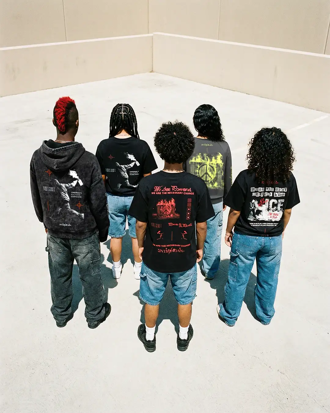 Group of people in graphic streetwear t-shirts and denim shorts standing in a sunlit urban lot