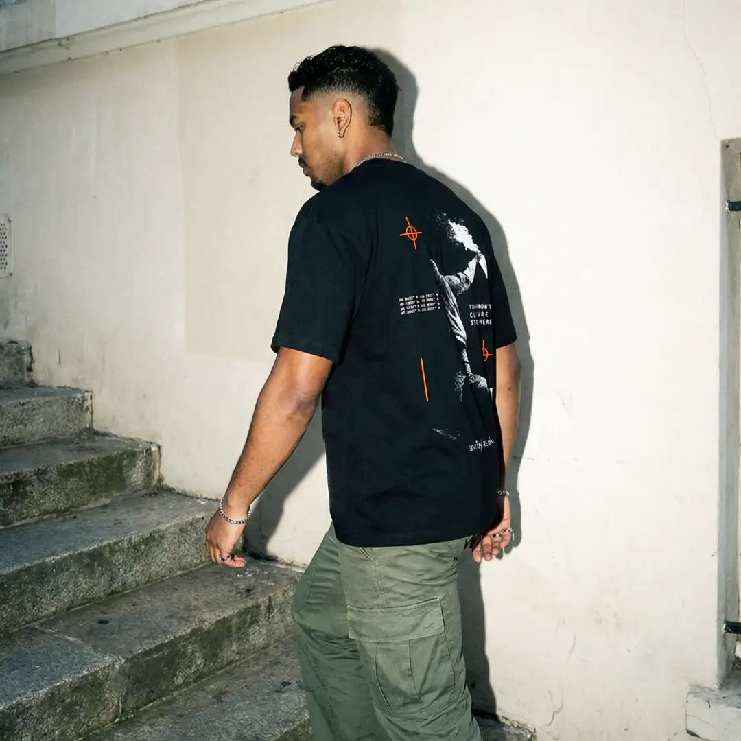 Man in graphic black streetwear t-shirt and green cargo pants walking up stone steps