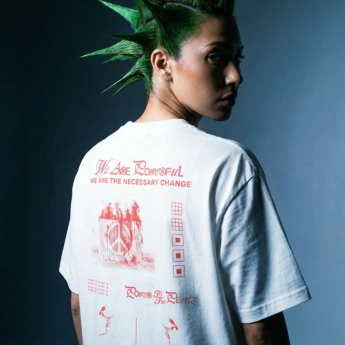 Person with spiked green hair wearing graphic white streetwear t-shirt with red text